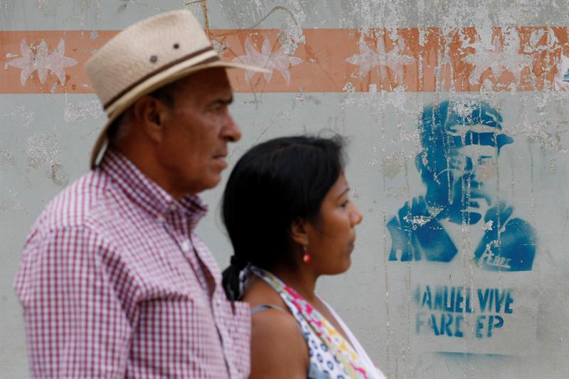 Dos personas pasan frente un pintada alusiva a uno de los fundadores de la guerrilla de las FARC, en Cauca, una de las zonas más afectadas por el conflicto. EFE | Confidencial