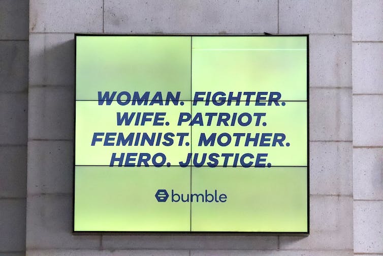 Una valla publicitaria que dice 'Mujer. Luchadora. Esposa. Patriota. Feminista. Madre. Héroe. Justicia.'