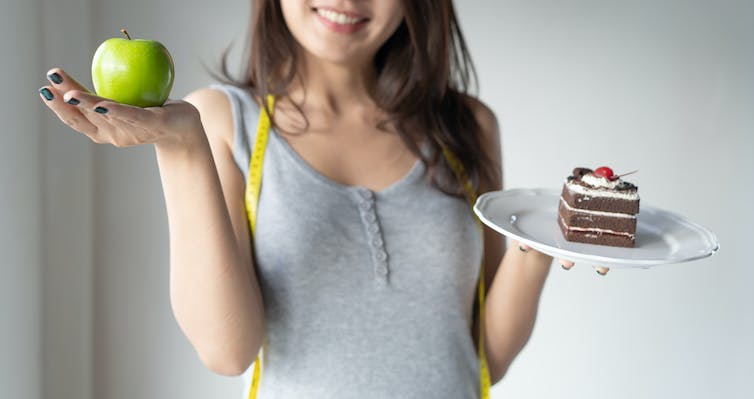 Una mujer levanta una manzana con una mano y baja un plato con tarta en la otra mano..