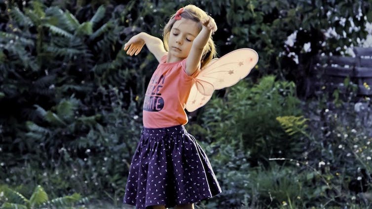 Una niña vestida con alas de hada baila en un jardín.