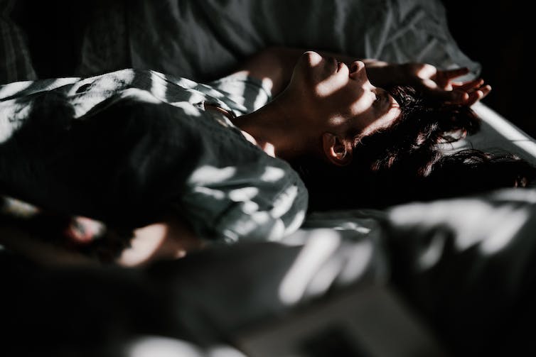 Mujer tumbada en la cama, con el sol entrando por las persianas