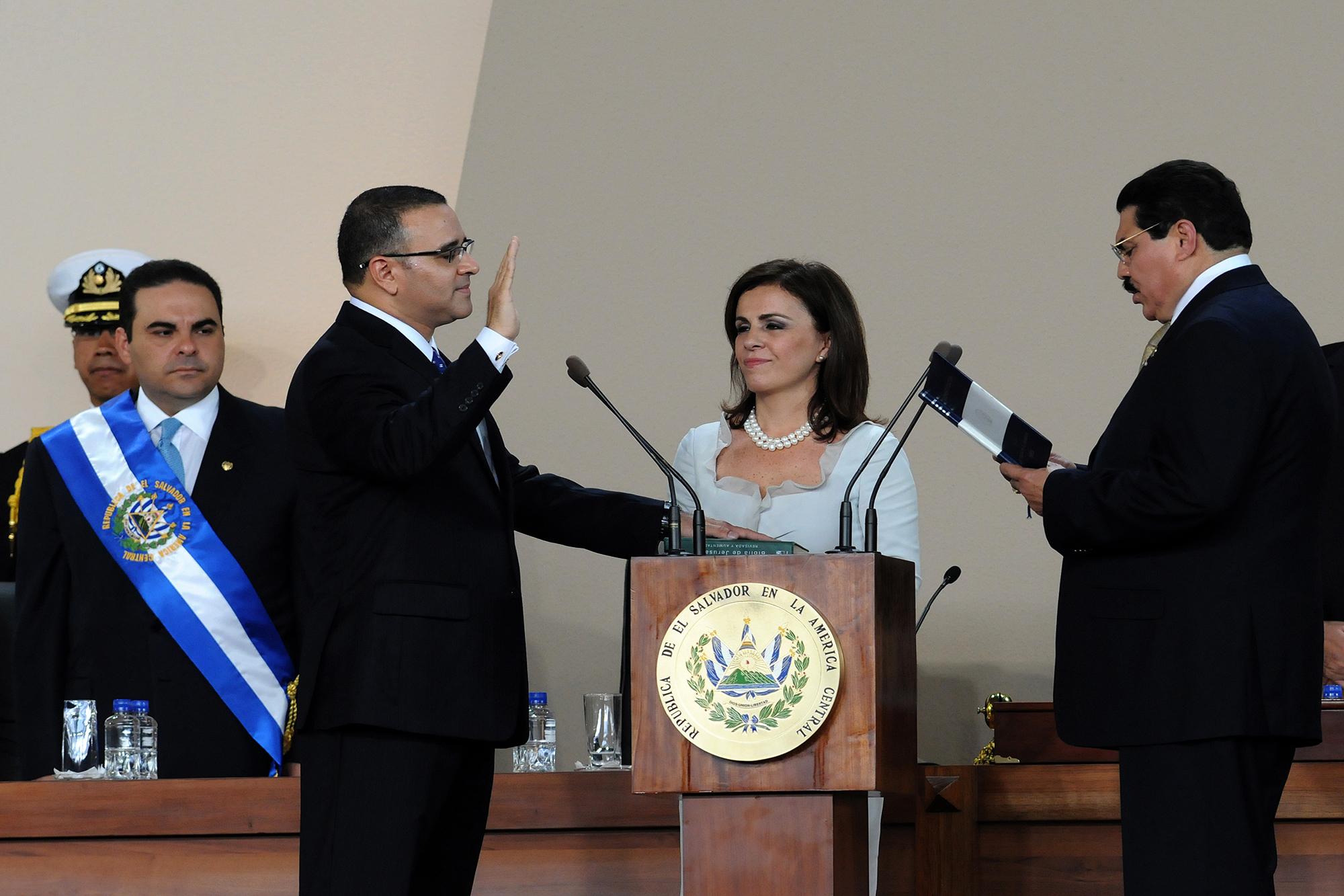 Imagen de la toma de posesión de Mauricio Funes como presidente de El Salvador ante el entonces presidente de la Asamblea Legislativa, Ciro Cruz Zepeda, el 1 de junio de 2009. En medio, su entonces esposa, Vanda Pignato. Atrás, aún con la banda presidencial, el ex presidente arenero Elías Antonio Saca, ahora condenado a diez años de prisión por peculado y lavado de dinero. Al igual que Funes, Saca fue acusado por haberse aprovechado de la partida de gastos reservados para beneficio personal. Foto de AFP: José Cabezas.